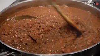 Dal Makhani simmering in a pan, showing creamy brown lentil curry with a wooden spoon stirring it.