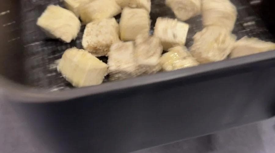 Tofu cubes in air fryer basket coated with oil before cooking.