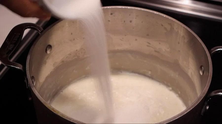Heavy cream being poured into a pot of simmering rice pudding on the stovetop.