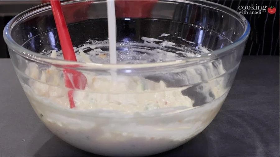 Waffle batter with cheddar cheese and chives being mixed in a glass bowl with two spoons.