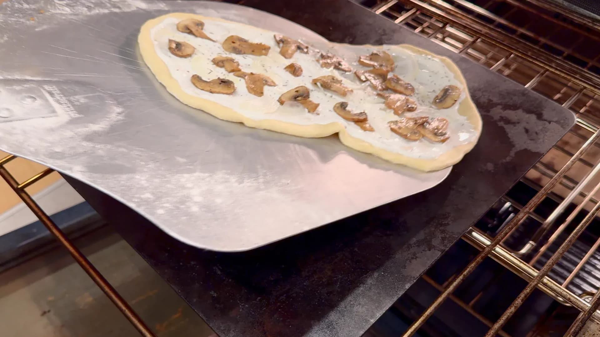 Flammkuchen dough topped with sautéed mushrooms and onions on parchment paper, ready to broil in the oven.