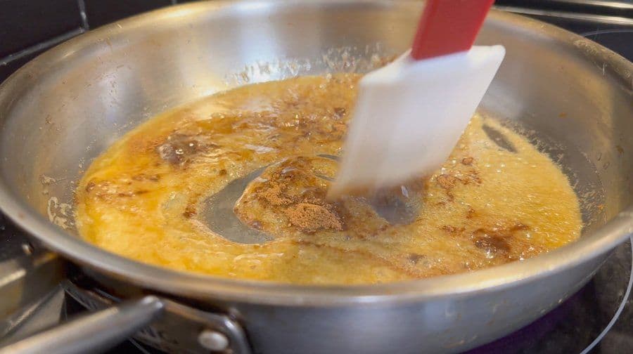 Spatula stirring golden caramel with brown sugar and spices in a pan on the stove.