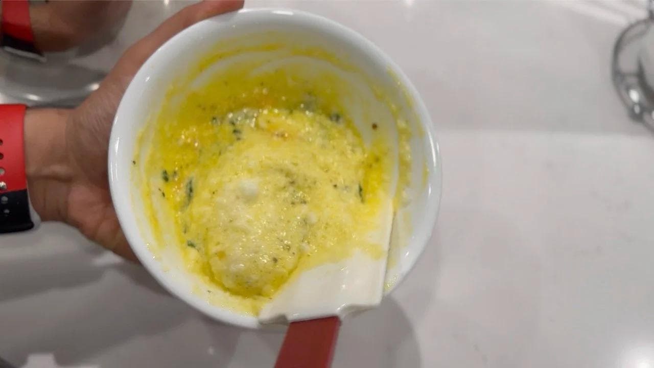Folded egg white and yolk mixture in white ramekin with melted butter and herbs, ready for baking.