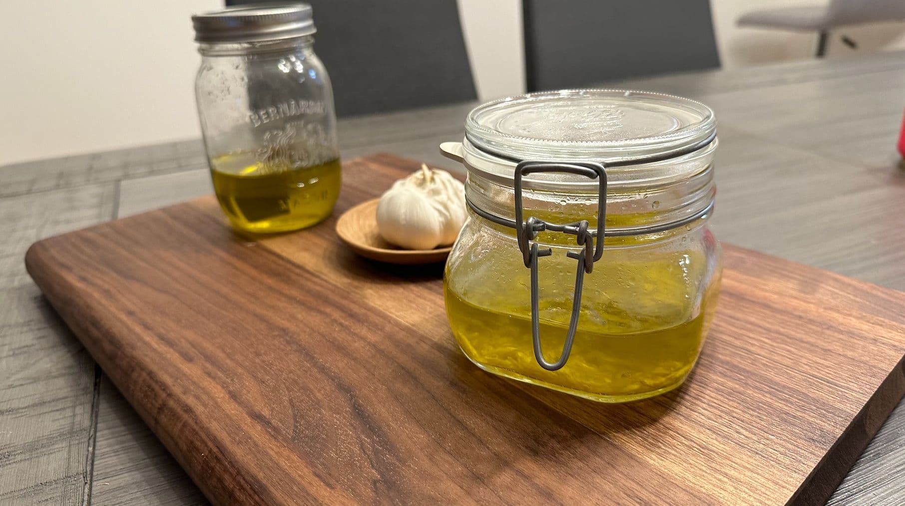 Homemade garlic-infused oil in glass jars on a wooden board with fresh garlic clove.