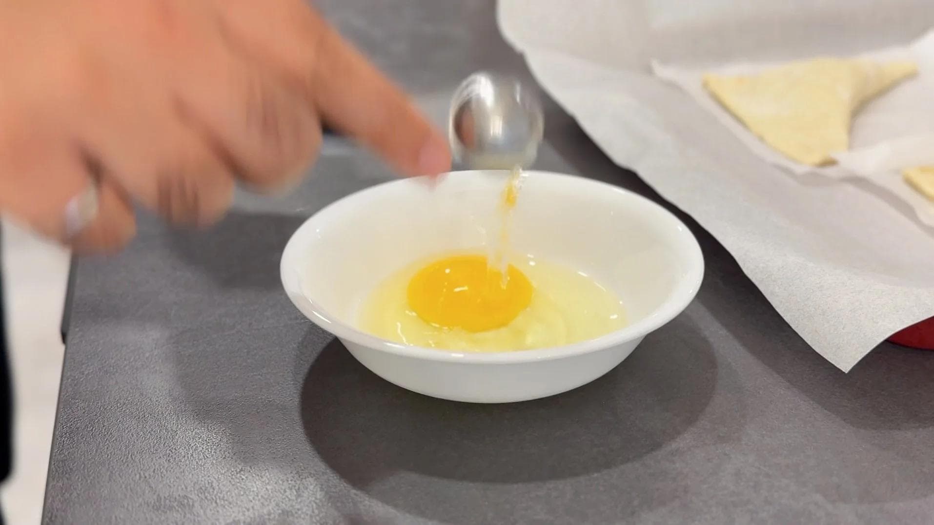 Whisking an egg in a white bowl with a fork, with parchment paper visible nearby.
