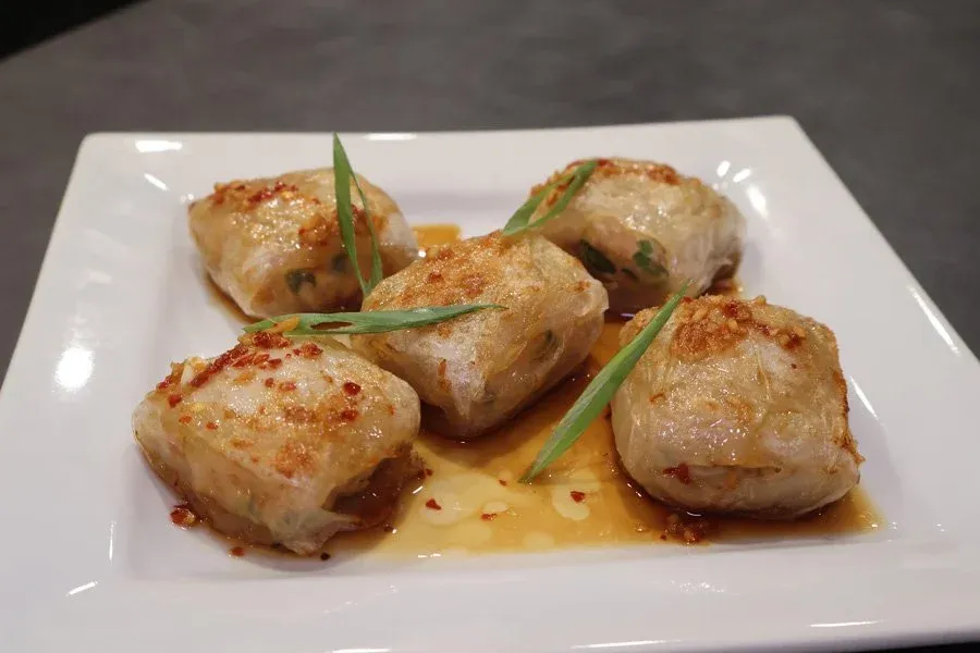 Four golden air fryer chicken dumplings on a white plate with sauce, garnished with green onions.