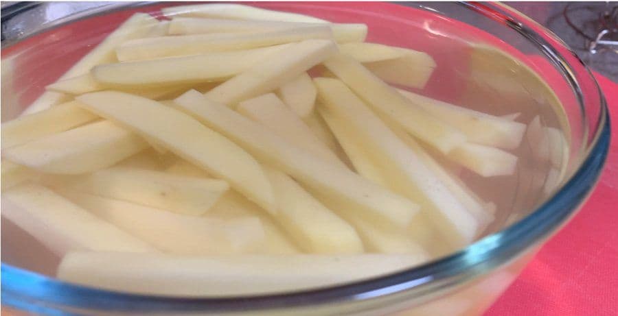 Peeled and cut potato fries soaking in cold water in a glass bowl.