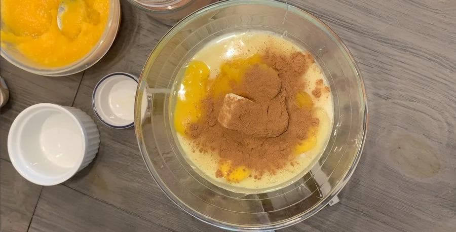 Pumpkin pie filling ingredients mixed in a glass bowl with cinnamon spice sprinkled on top, ready to pour into crust.