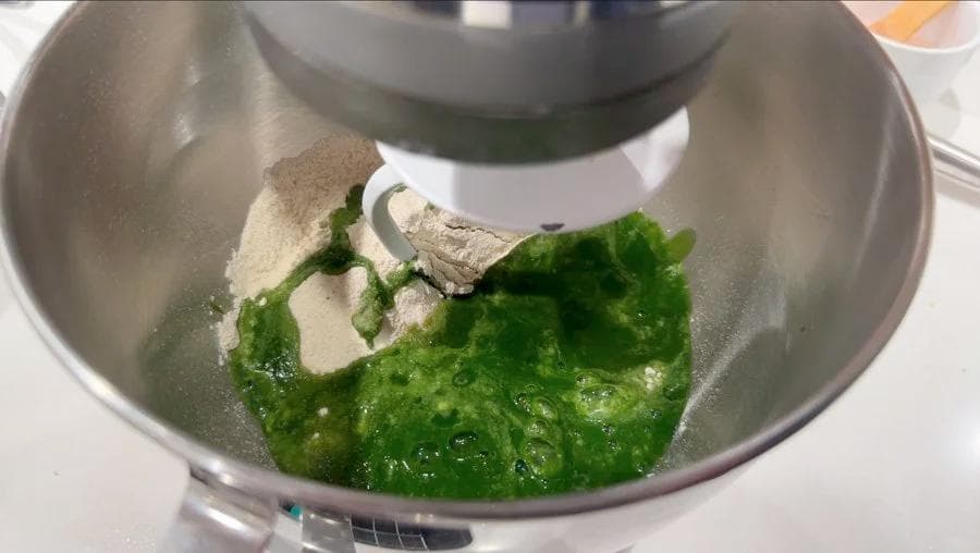 Spinach and flour being mixed in a stainless steel bowl with a dough hook attachment during palak paratha preparation.