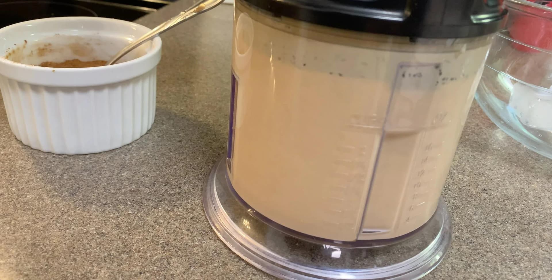Blended pumpkin spice frappuccino in a food processor with tan-colored mixture and crushed ice visible.