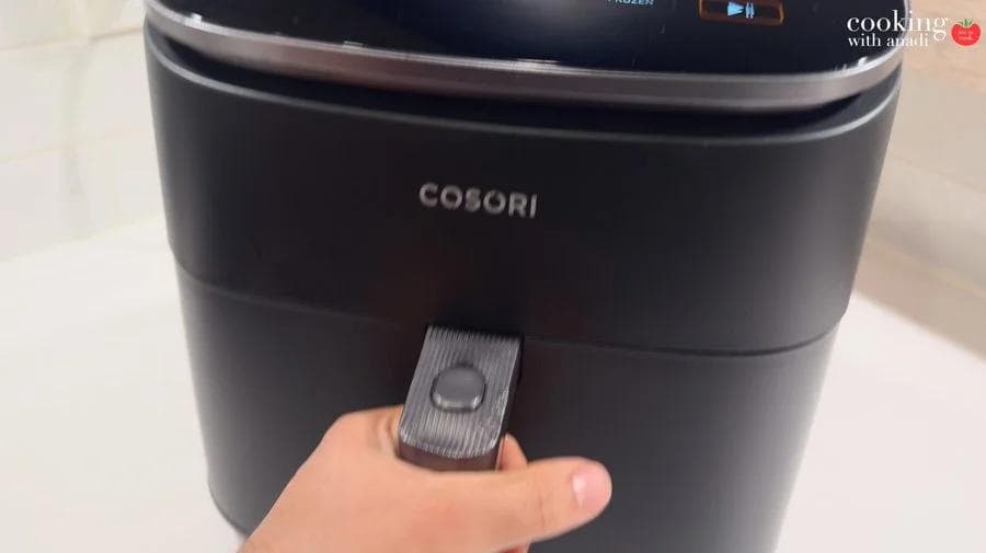 Hand pulling open the basket drawer of a black Cosori air fryer