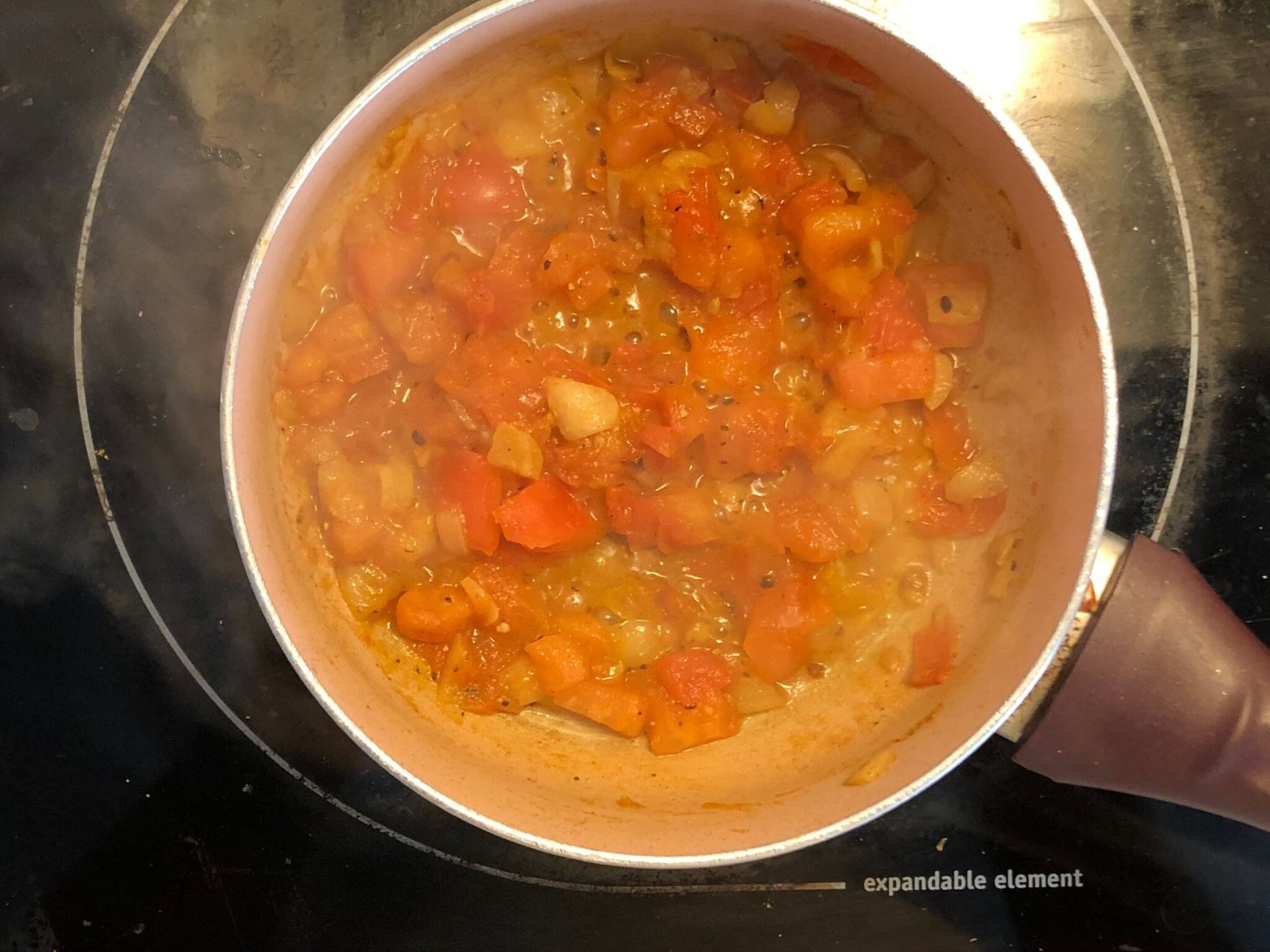 Tomato-based curry mixture simmering in a pot with diced vegetables and spices.