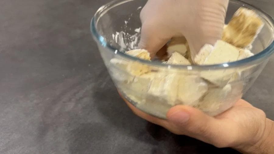Hands mixing tofu cubes with cornstarch and seasonings in a glass bowl