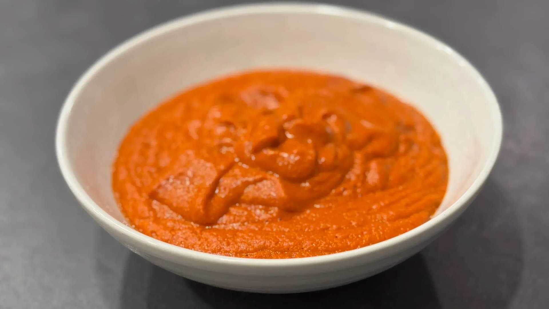 Spicy red momo chutney in a white bowl with chunks of ingredients visible in the smooth sauce.