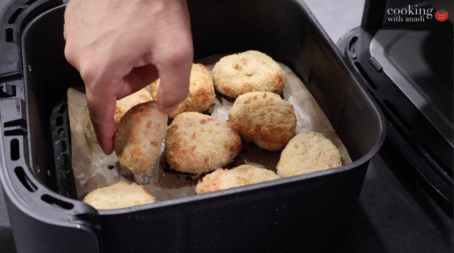 Golden-brown air fryer chicken nuggets in a black air fryer basket, being removed with tongs.