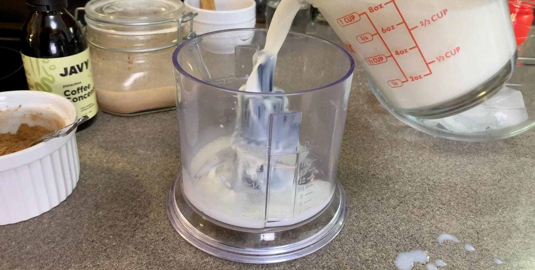 Food processor filled with milk, ice, and pumpkin sauce being blended for a pumpkin spice frappuccino.