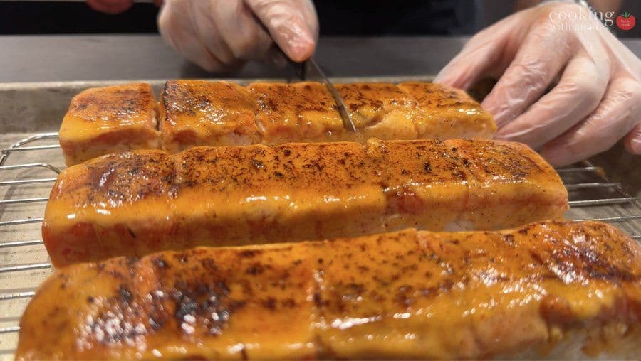 Torched oshizushi pieces with deep golden-brown char and caramelized salmon tops being cut with a knife.