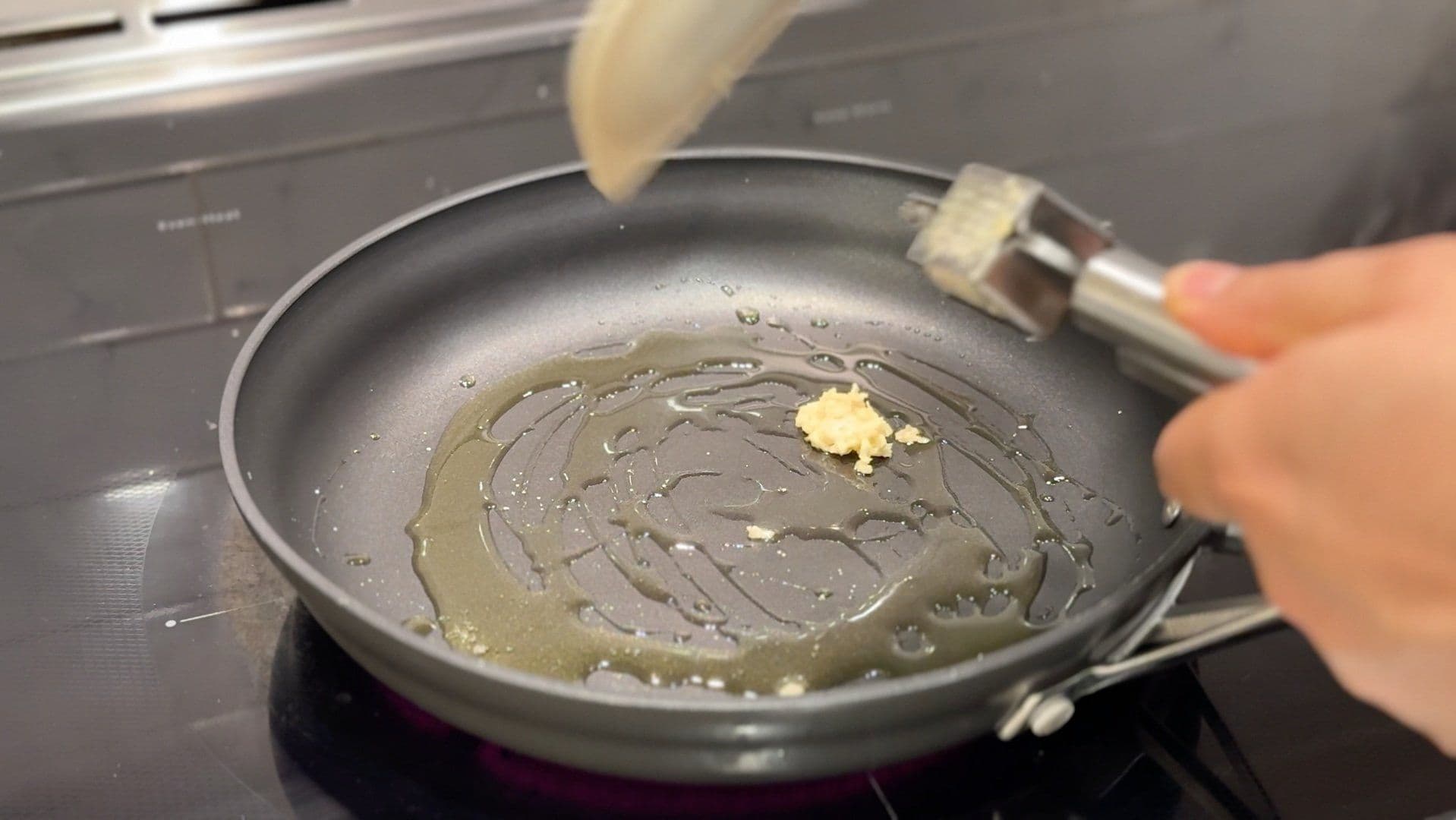 Garlic and chili flakes sautéing in olive oil in a frying pan on a stovetop.