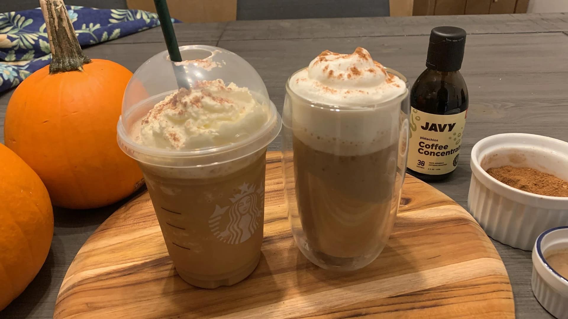 Two homemade pumpkin spice frappuccinos with whipped cream and cinnamon, served with fresh pumpkins and coffee concentrate.