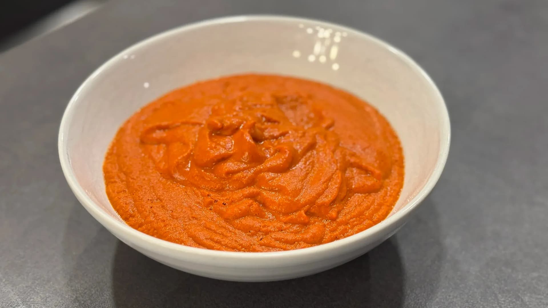 Spicy momo chutney in a white bowl, showing a smooth, vibrant orange-red sauce texture.
