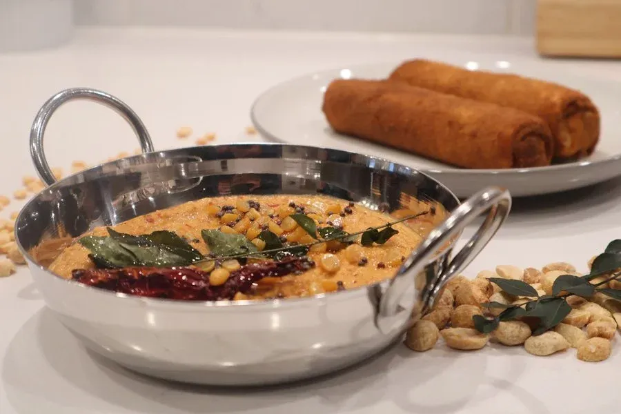 South Indian roasted peanut chutney served in a stainless steel bowl with curry leaves and tempering, alongside vada and cashews.