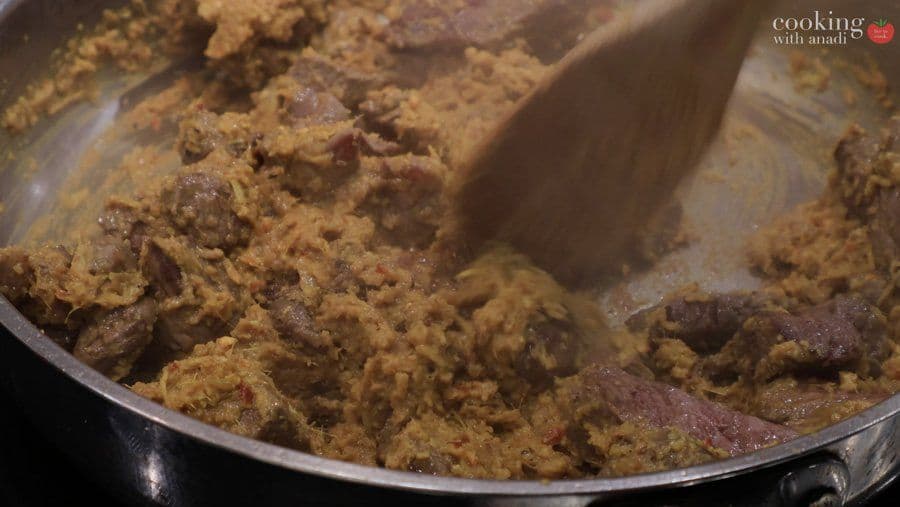 Beef rendang paste being stirred in a pan with a spatula, showing the cooked spice mixture and meat pieces.