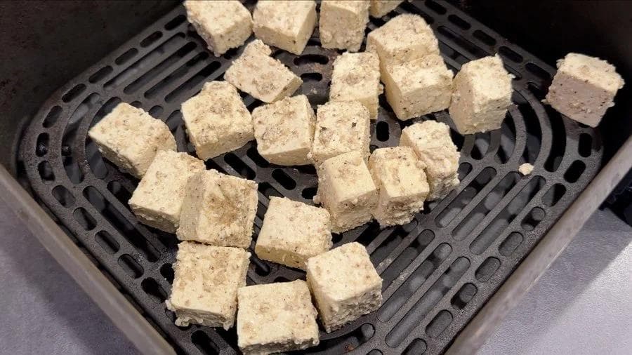 Tofu cubes arranged in a single layer in an air fryer basket before cooking.
