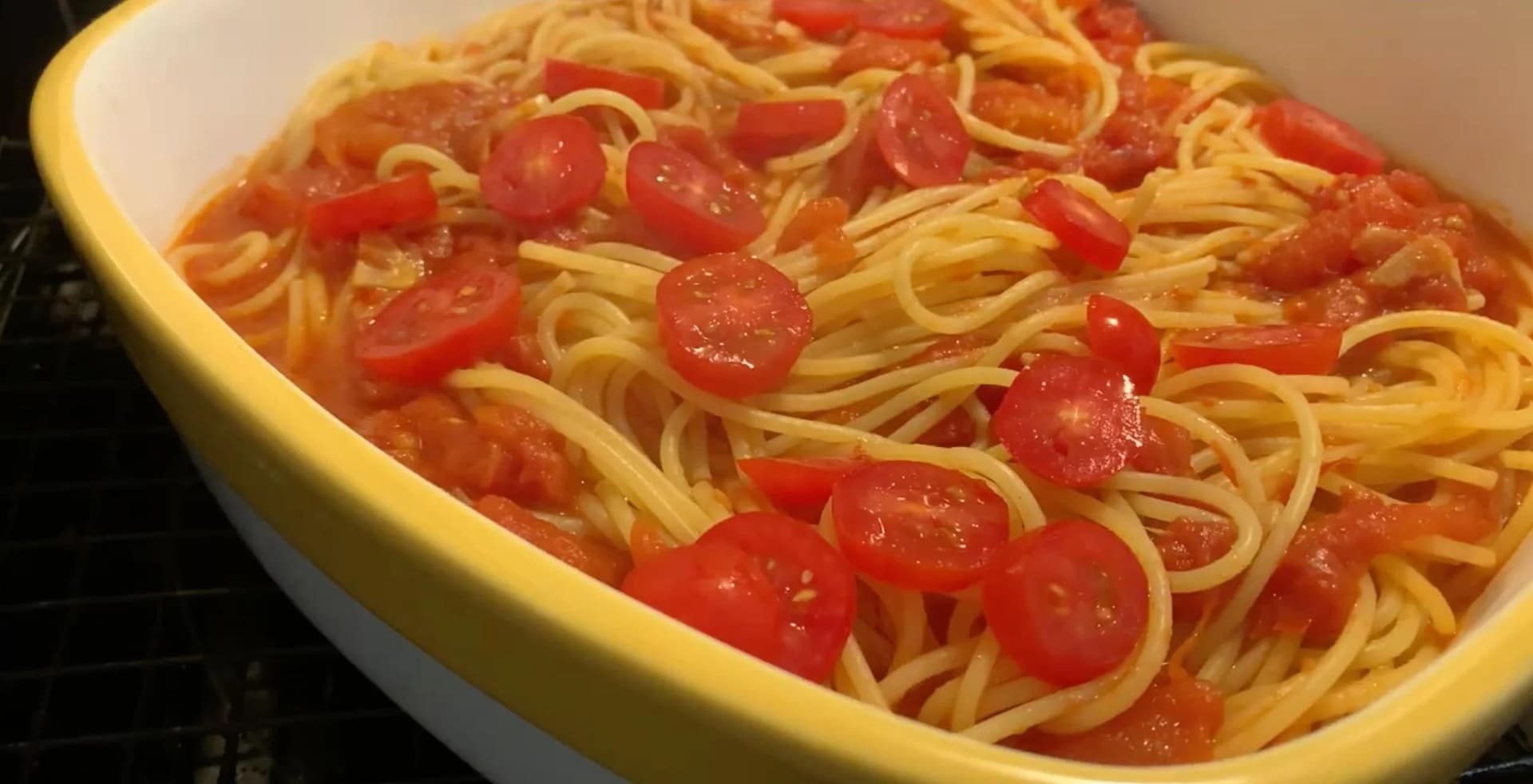 Spaghetti with tomato sauce and fresh tomatoes in a yellow-rimmed white casserole dish, ready to bake.