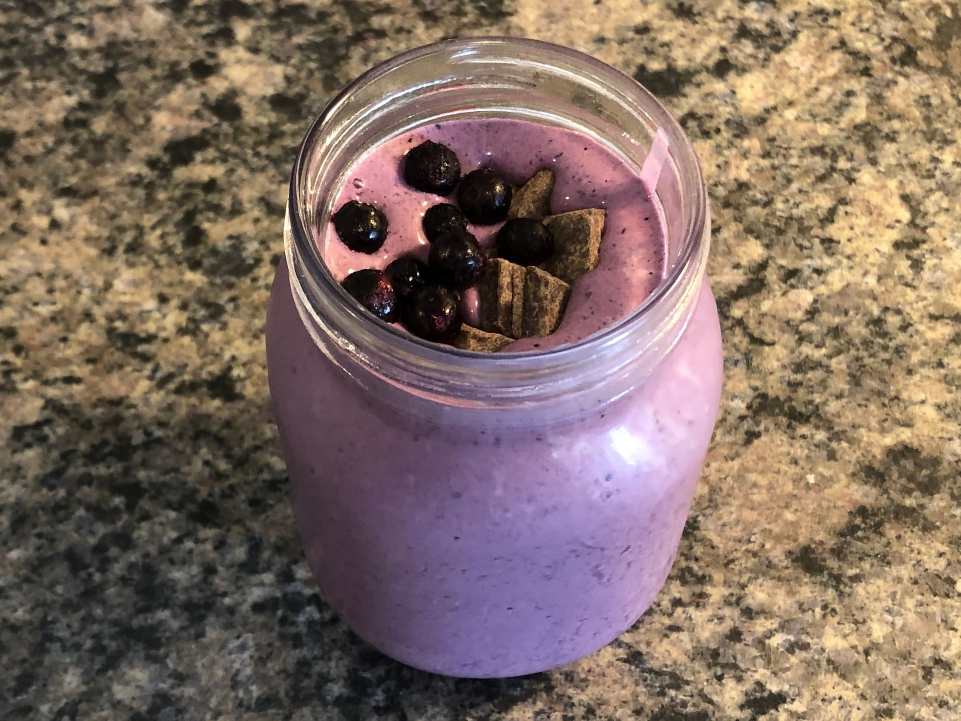 Creamy blueberry protein smoothie in a glass jar topped with fresh blueberries and chocolate pieces.
