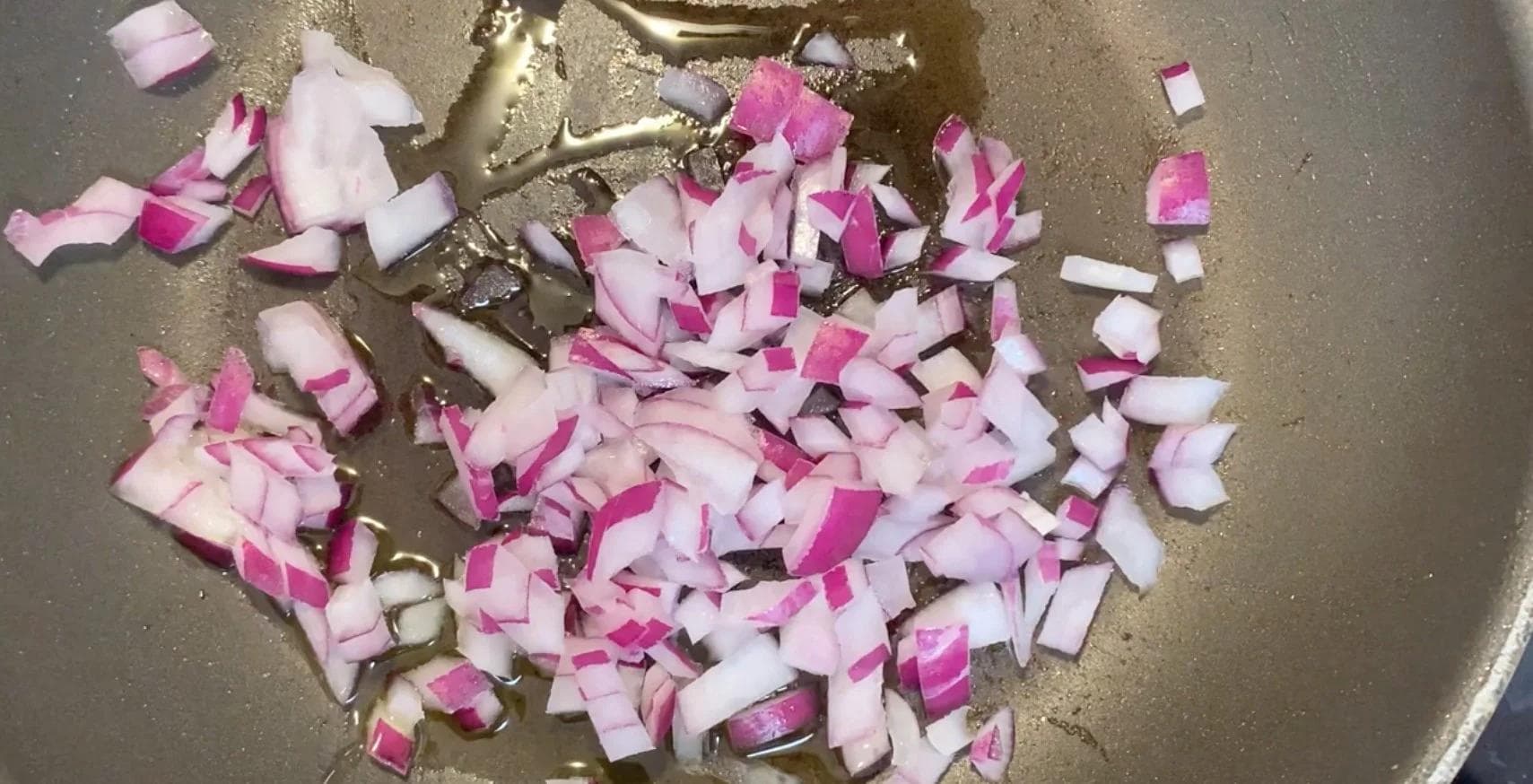 Chopped pink and white onions sautéing in a pan with garlic and oil.