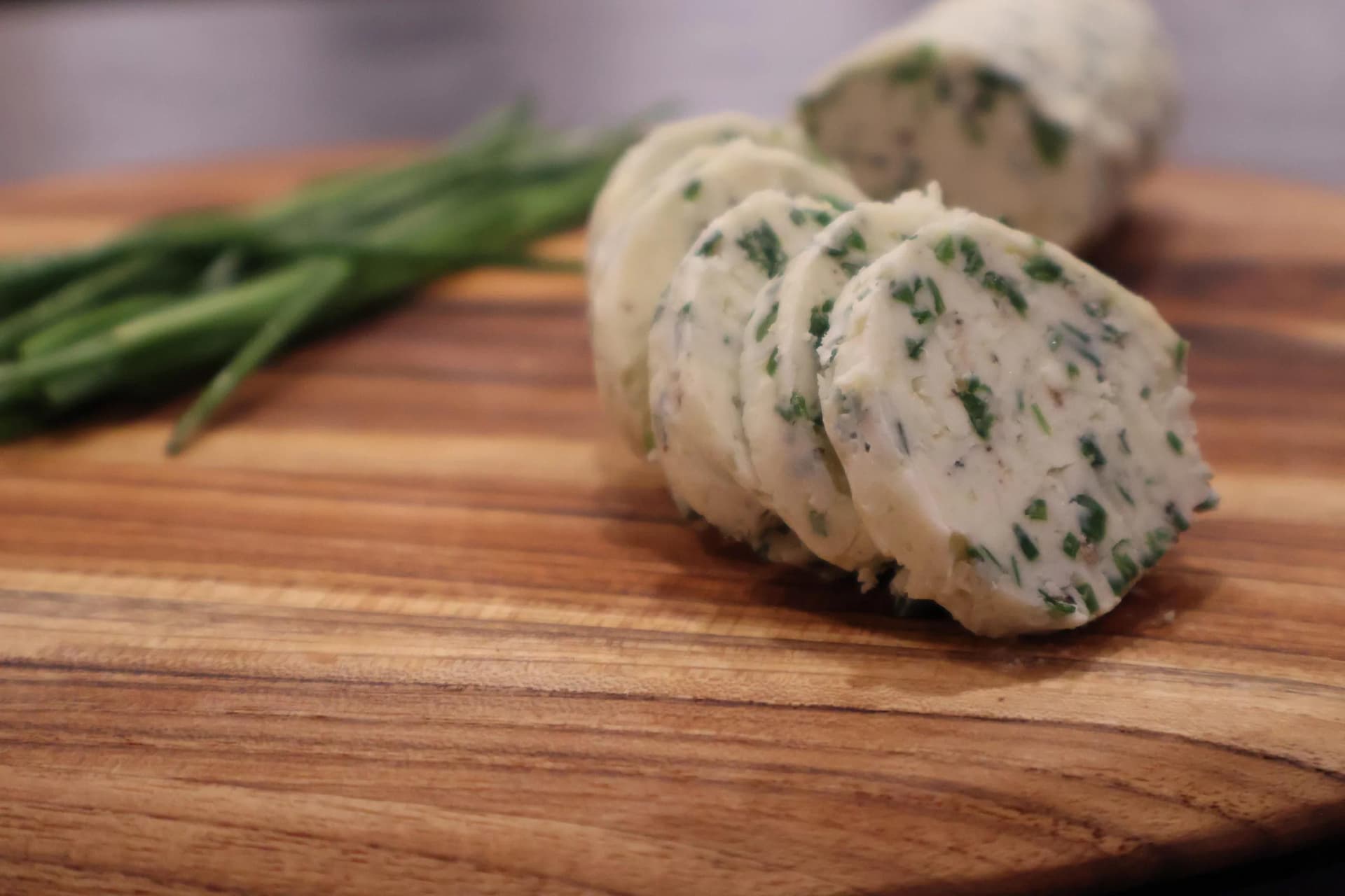 Sliced garlic herb butter with fresh chives on a wooden cutting board.