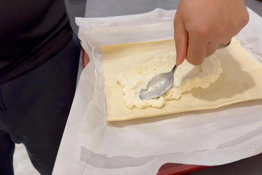 Spreading ricotta mixture over puff pastry with a spatula on parchment paper.
