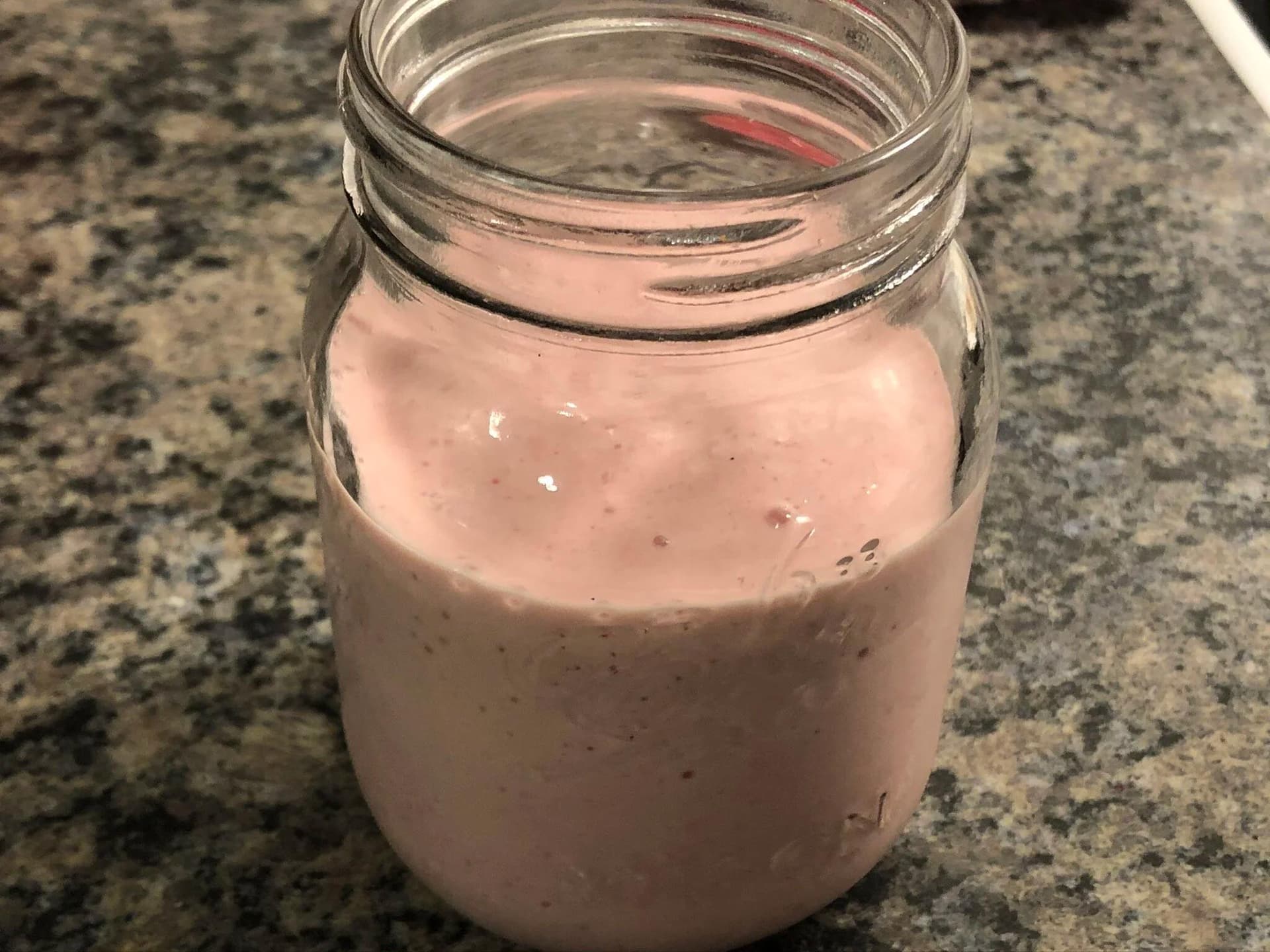Pink strawberry cheesecake smoothie in a mason jar on a granite countertop.