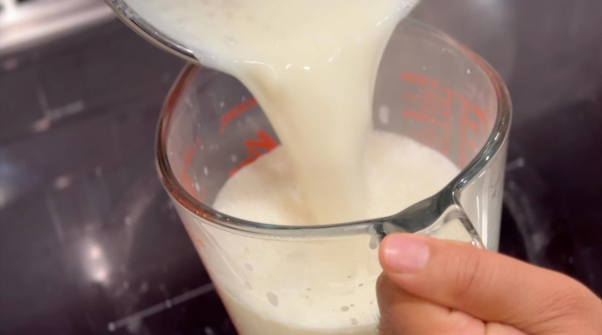 Chilled rose-flavored milk being poured into a measuring cup for Indian Falooda recipe.