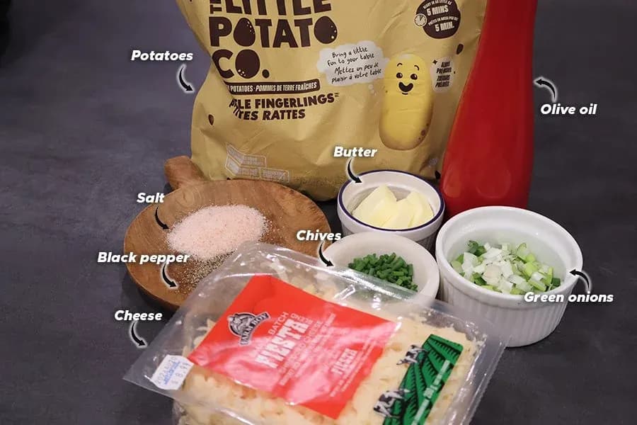 Ingredients for air fryer smashed potatoes laid out including fingerling potatoes, butter, cheese, chives, green onions, salt, pepper, and olive oil.