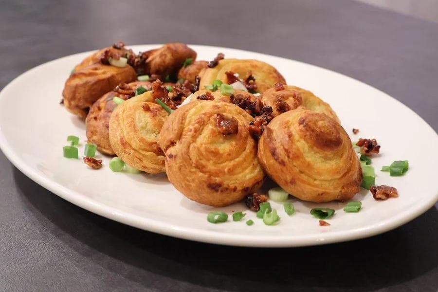 Golden air fryer mashed potato pinwheels topped with crispy bacon bits and green onions on a white plate.