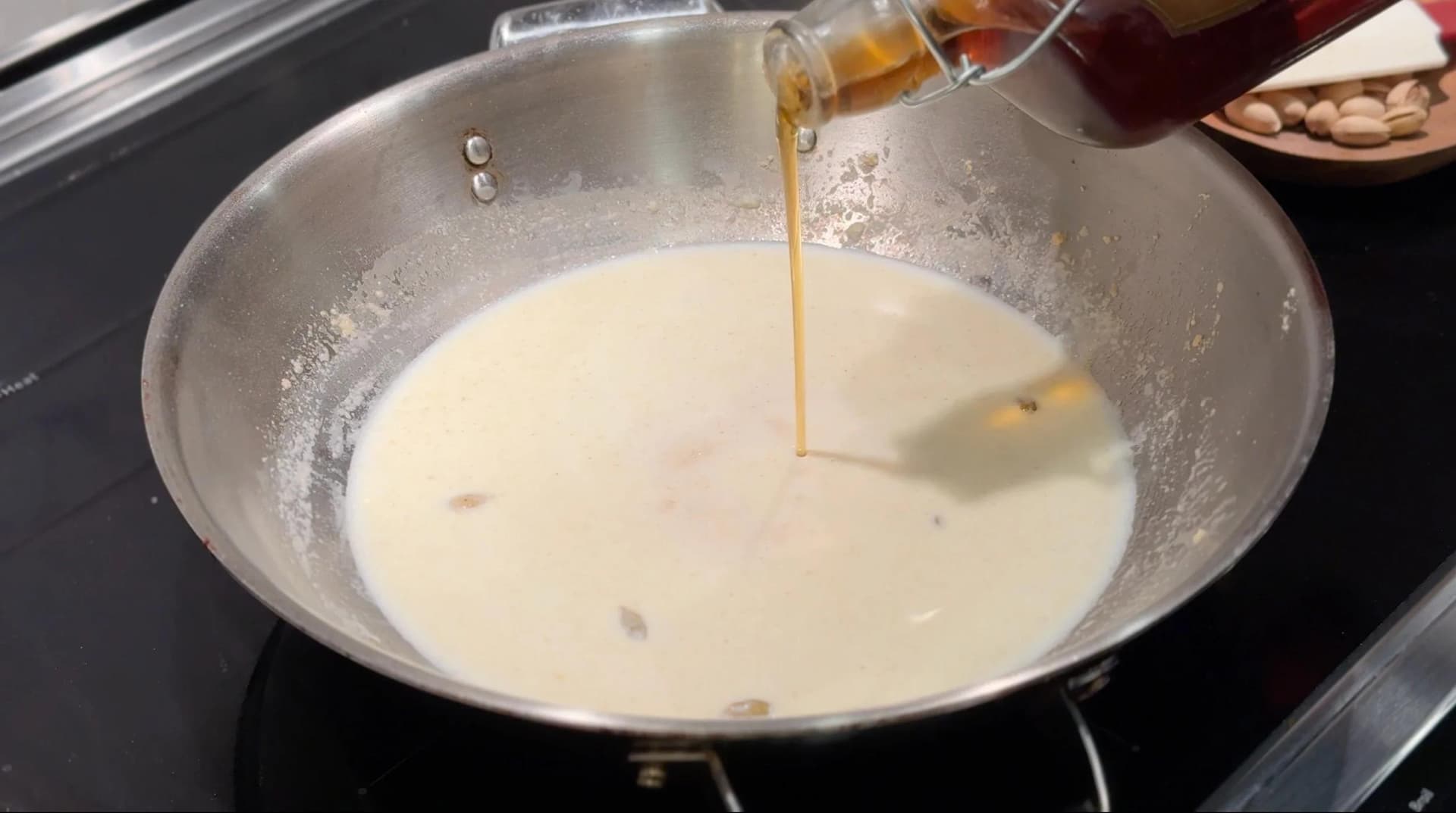 Golden liquid being poured into creamy semolina milk mixture in a pot on stovetop.