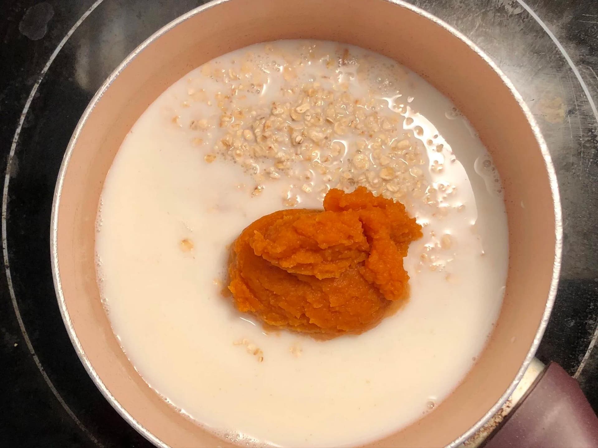 Pumpkin puree and oats added to milk in a pot before mixing together