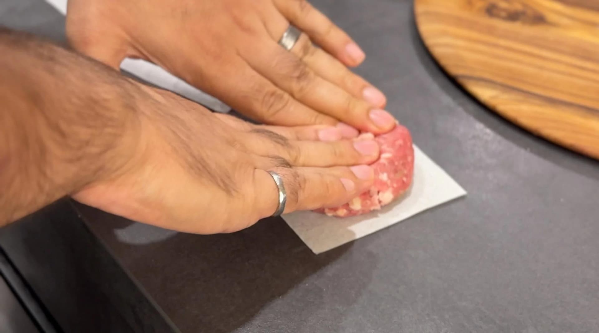 Hands pressing ground beef patty onto parchment paper to form a burger slider patty.