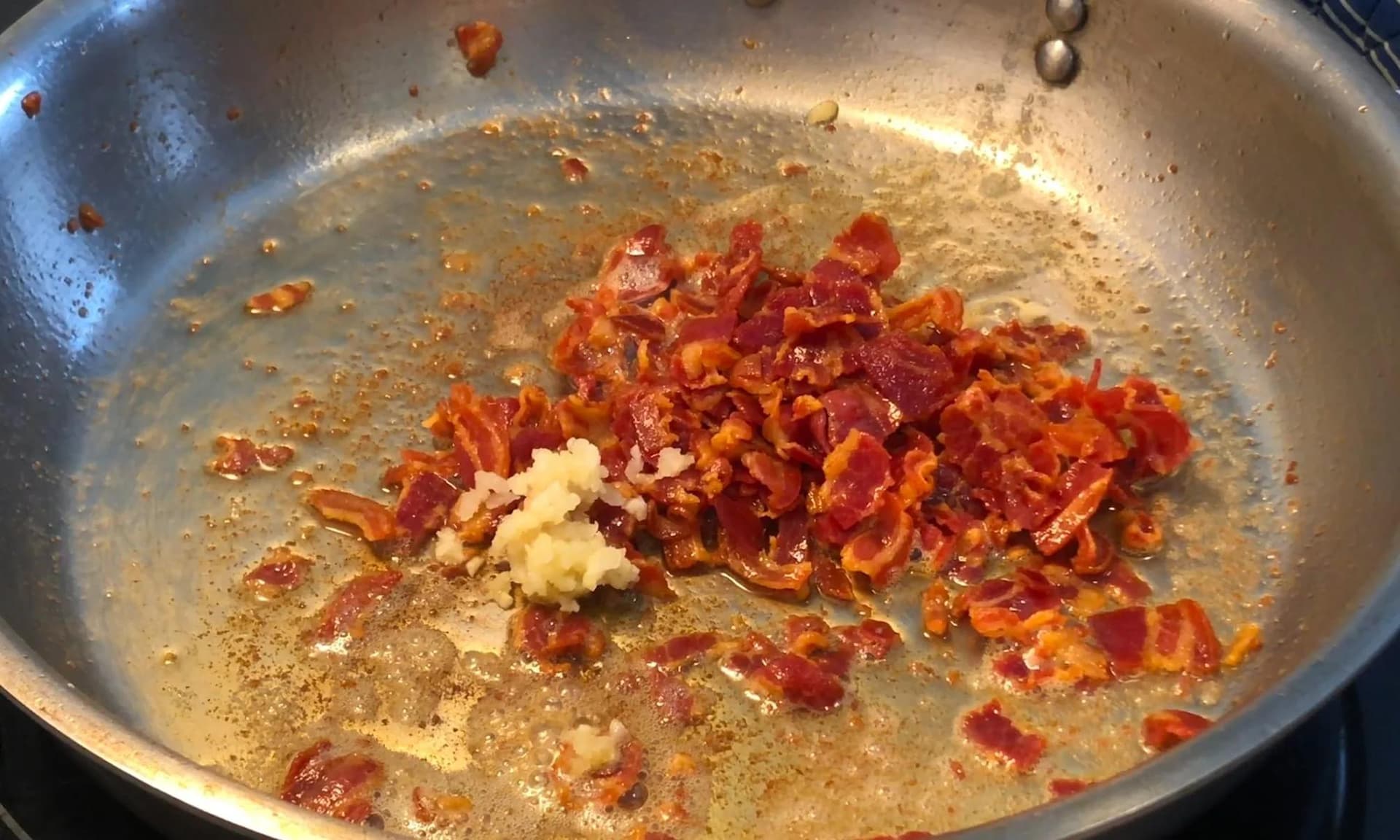Crispy pancetta and minced garlic sautéing in butter in a stainless steel pan.