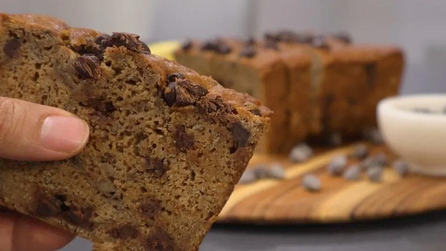 Hand holding a slice of gingerbread banana bread with chocolate chips, showing moist crumb structure.