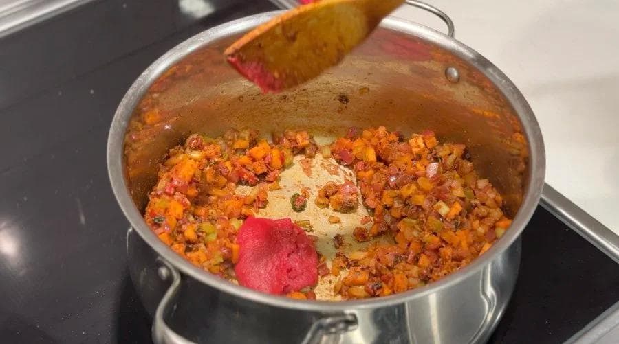 Tomato paste added to a pot of cooked lentils and vegetables, ready to be stirred in while cooking.