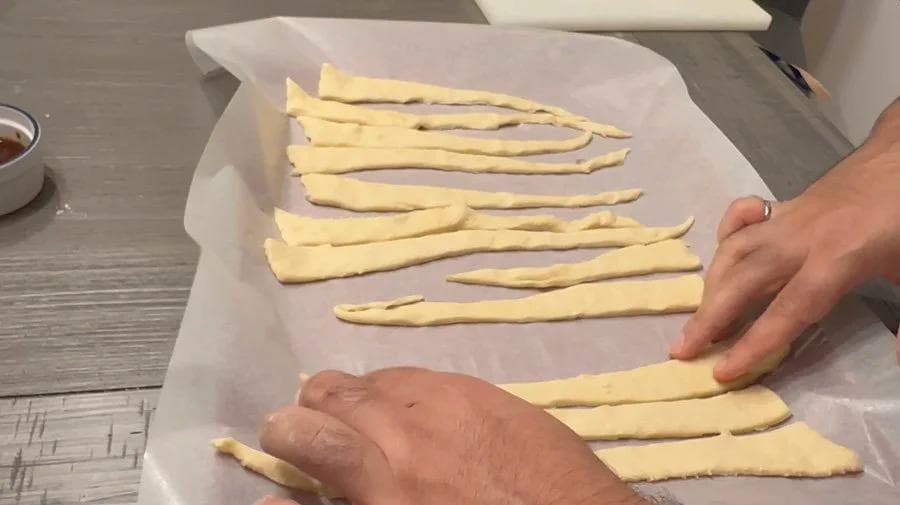 Crescent roll dough strips laid out with sausages being wrapped inside before air frying.