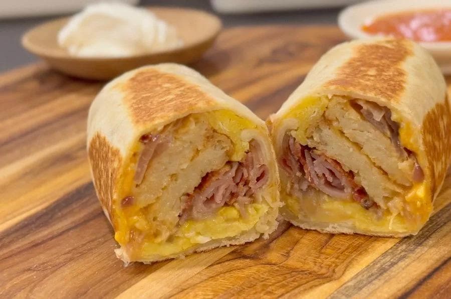Breakfast burrito cut in half showing scrambled eggs, ham, and melted cheese on toasted bread.