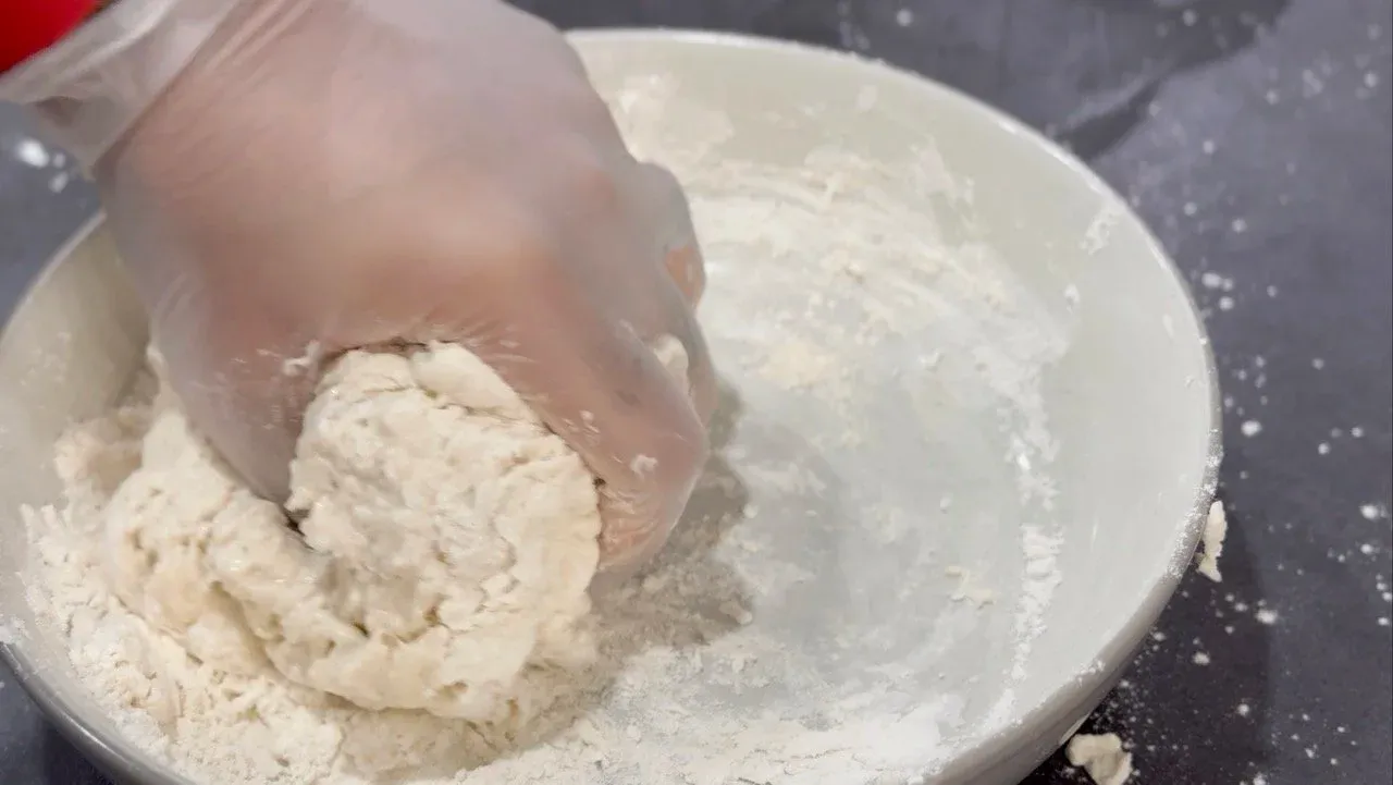 Hand kneading soft momo dough in a white bowl with flour dusted on the surface.