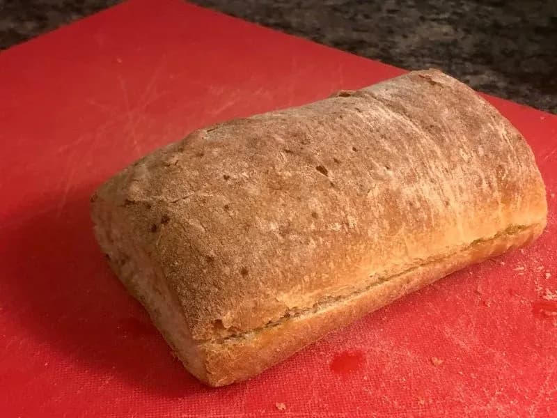 Toasted ciabatta roll with golden-brown exterior on red surface, ready for chicken parmesan assembly.
