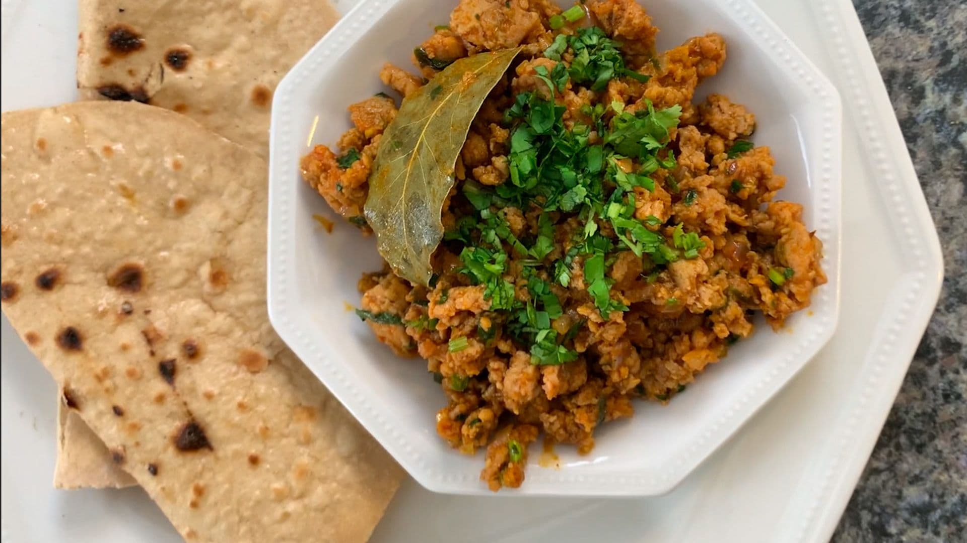 Spiced ground chicken keema garnished with cilantro and bay leaf, served with warm flatbread.