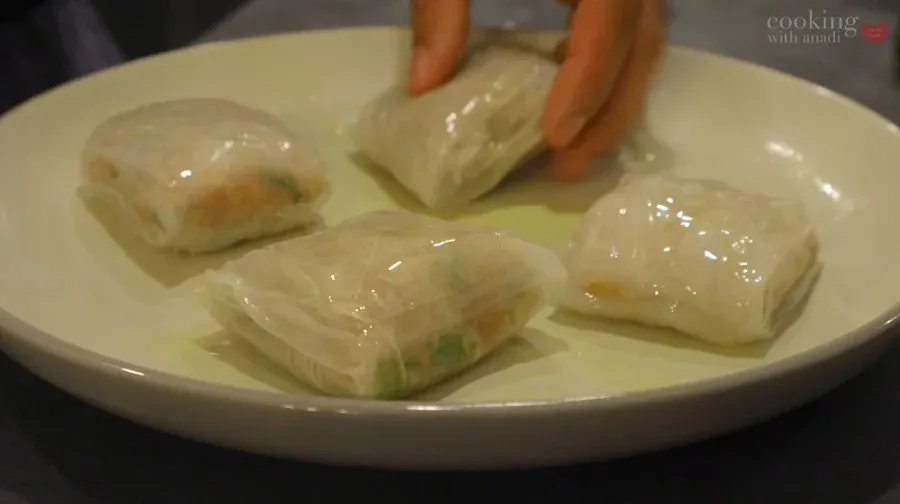Four translucent rice paper dumplings arranged on a white plate with sauce, being plated with chopsticks.