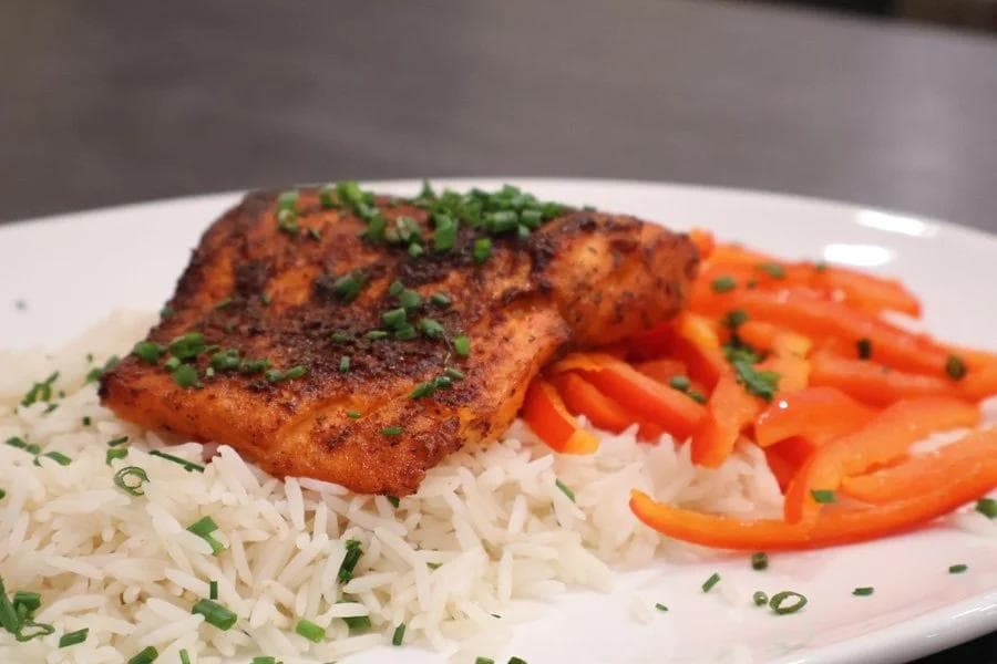 Air fryer salmon fillet with crispy seasoned exterior served over white rice with red bell pepper strips and green onion garnish.