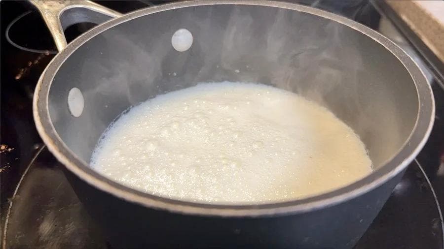Steaming milk with red velvet mixture in a pot, ready to be frothed for a latte.